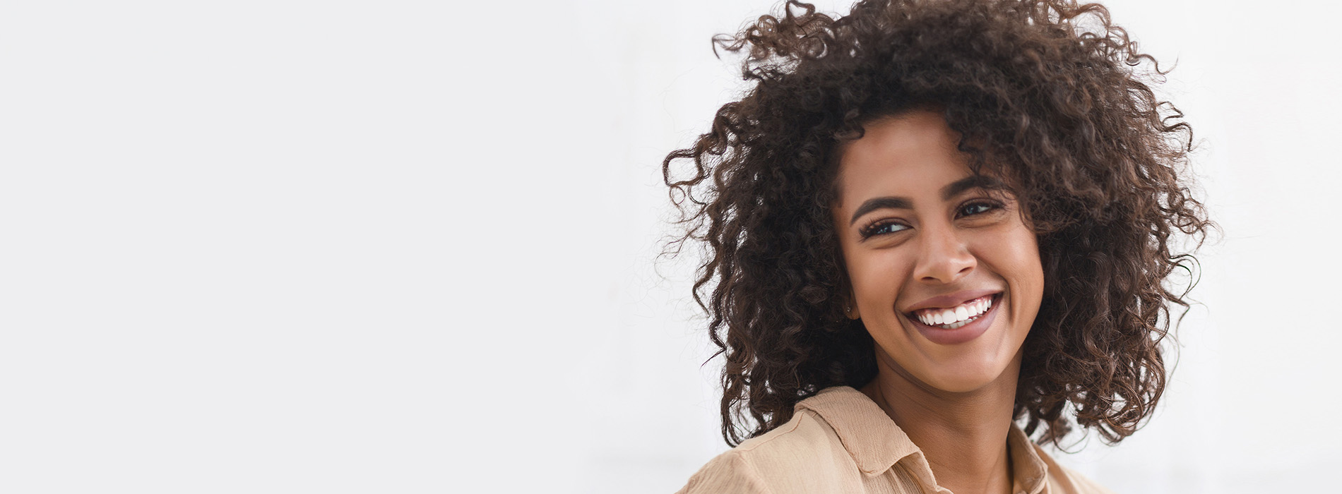 The image is a photograph of a woman with light skin, smiling at the camera. She appears to be in her late twenties or early thirties and has long hair. Her eyes are looking directly at the camera, and she is holding up her index finger near her mouth as if she s making a point or emphasizing something. The background is plain and light-colored, which suggests that this could be a stock photo used for various purposes such as advertising, personal branding, or lifestyle content.